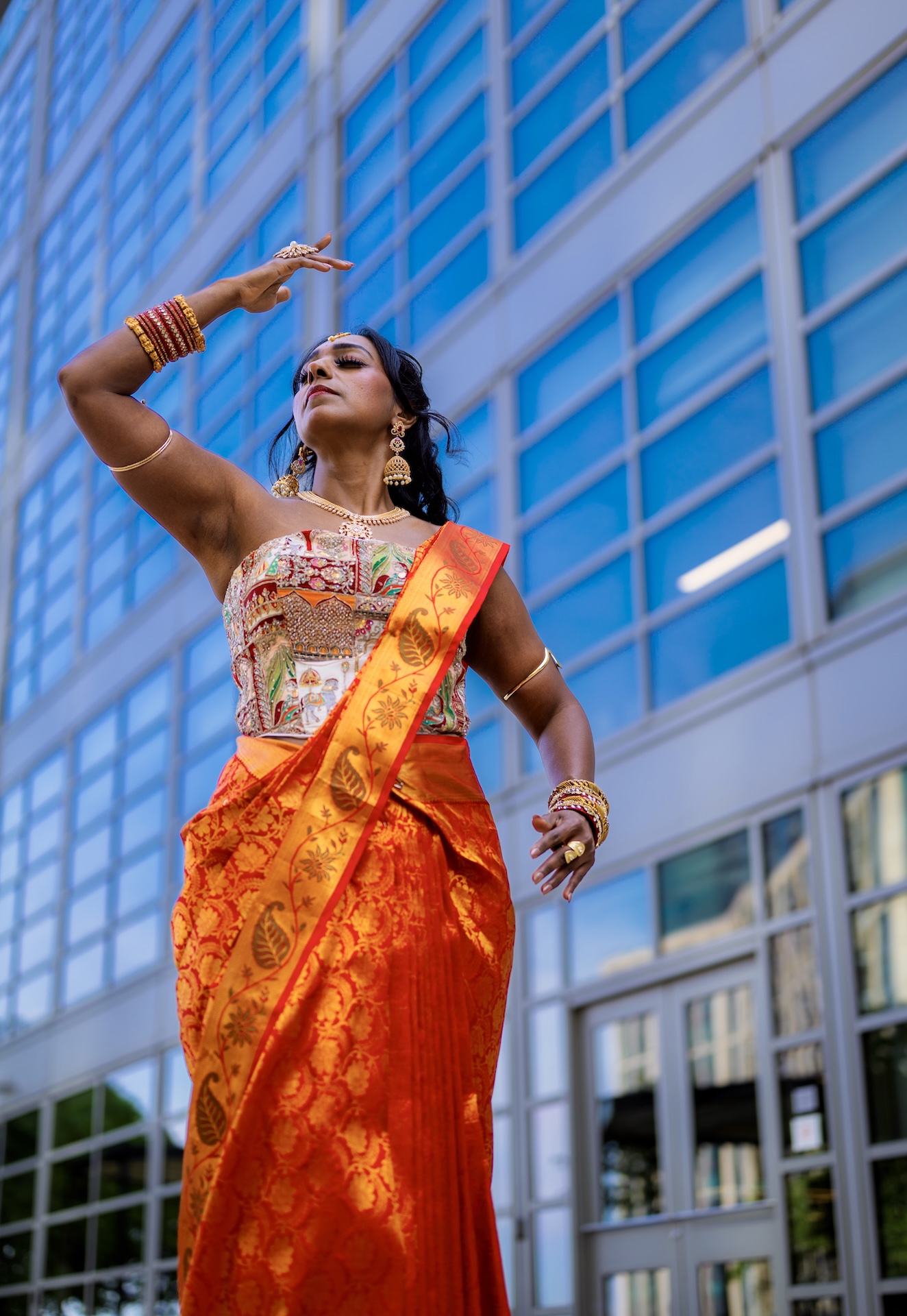 Classical dance pose in an orange silk saree against blue glass — Vetri Frames, the DMV